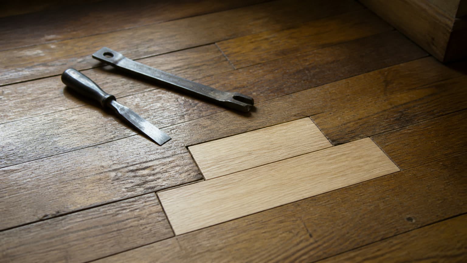 A damaged section of hardwood flooring cut out and replacement boards being woven into the surrounding floor