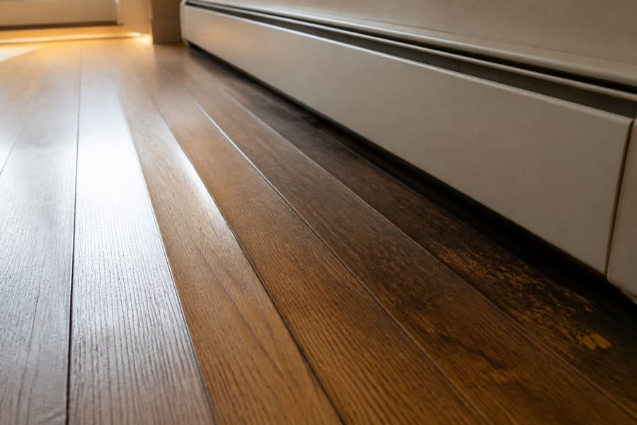 Hardwood boards cupped and darkened where water has reached them near a radiator